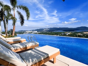 A poolside area with lounge chairs and a view of a body of water and distant landscape.