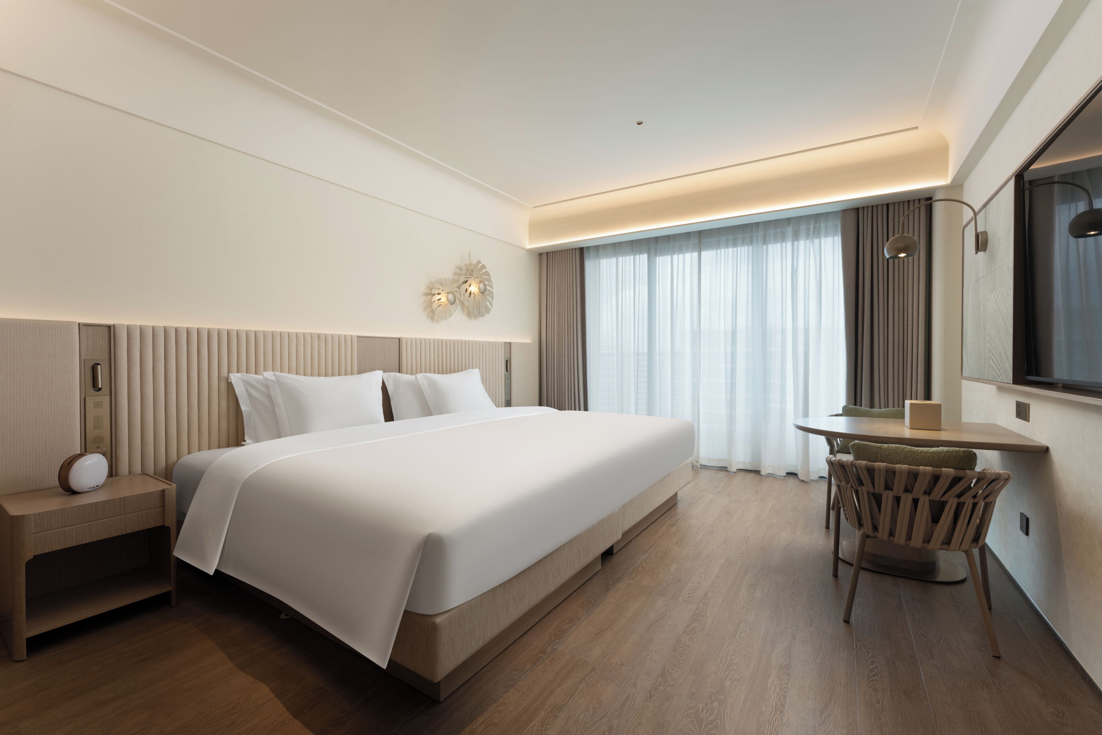 Une chambre d’hôtel moderne avec un grand lit, une table de chevet, une lampe et un petit coin repas avec une chaise.