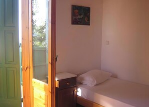 Une chambre à coucher avec un lit, une table de chevet, un tableau accroché au mur et une porte entrouverte donnant sur un espace extérieur.