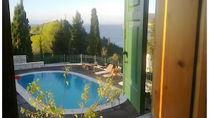 A pool with a view of trees and hills, a table with chairs, and a green door. - Apartment 'Villa Milia - Sea View' with Sea View, Wi-Fi and Air Conditioning (Lefkada)