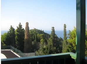 Blick von einem Balkon mit Steinmauer, Metallgeländer und verschiedenen Bäumen.