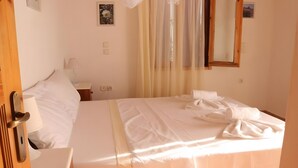 A hotel room with a bed, a bedside table with a lamp, a mirror, and a window with sheer curtains. - Apartment 'Villa Milia - Sea View' with Sea View, Wi-Fi and Air Conditioning (Lefkada)
