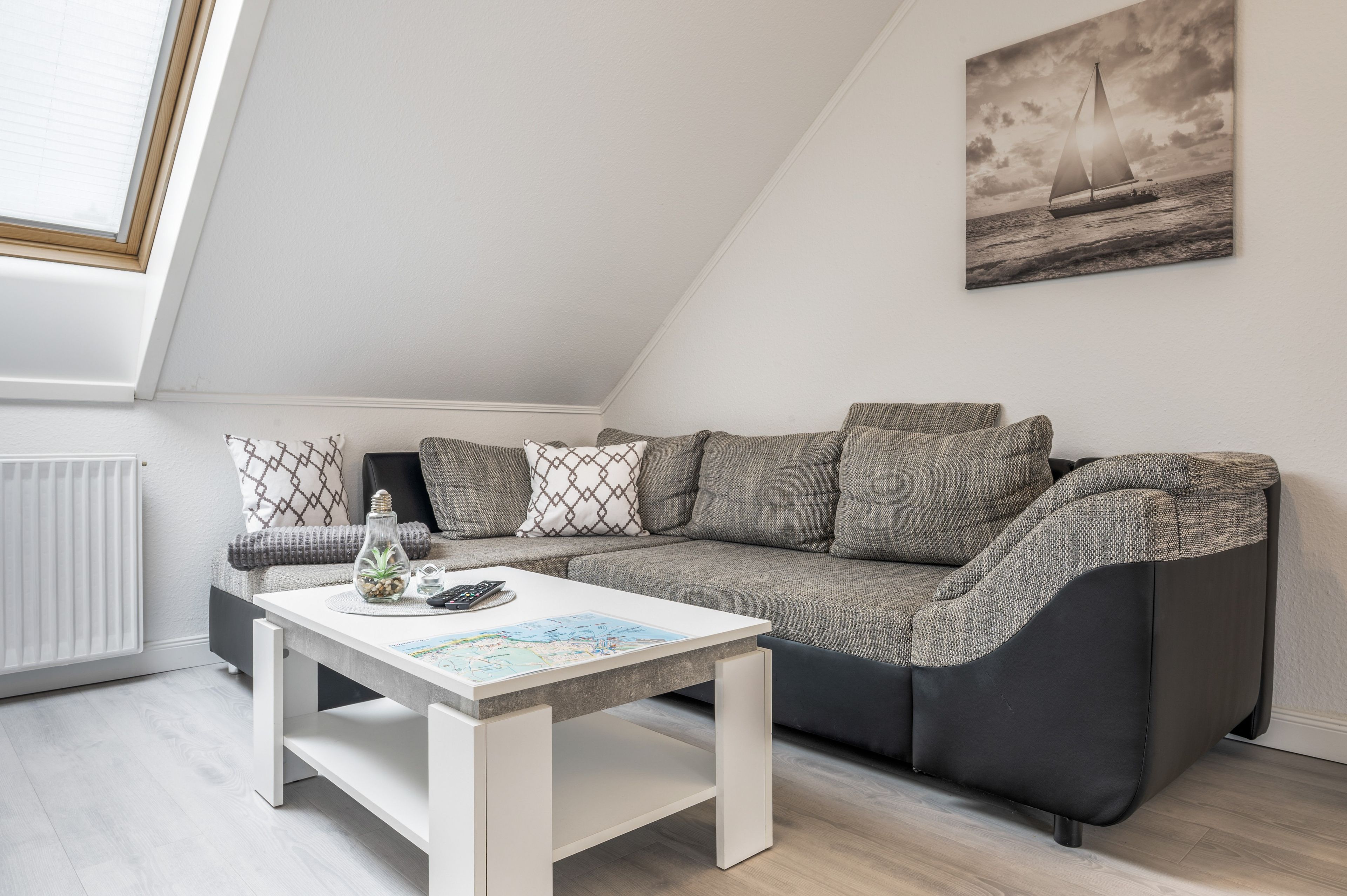 Una sala de estar moderna con un sofá gris, una mesa de centro blanca y un cuadro de un velero en la pared.