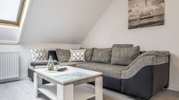 Una sala de estar moderna con un sofá gris, una mesa de centro blanca y un cuadro de un velero en la pared.