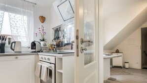 A modern kitchen with white cabinetry, a coffee machine, and a window with lace curtains. - Apartment “Seepferdchen” with Wi-Fi (Cuxhaven)