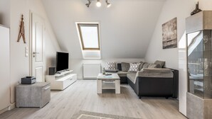 A modern loft-style living space with a sloped ceiling, a skylight, a flat-screen TV, a sofa, a coffee table, and a glass cabinet. - Apartment “Seepferdchen” with Wi-Fi (Cuxhaven)