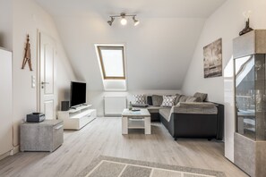 A modern loft-style living space with a sloped ceiling, a skylight, a flat-screen TV, a sofa, a coffee table, and a glass cabinet. - Apartment “Seepferdchen” with Wi-Fi (Cuxhaven)