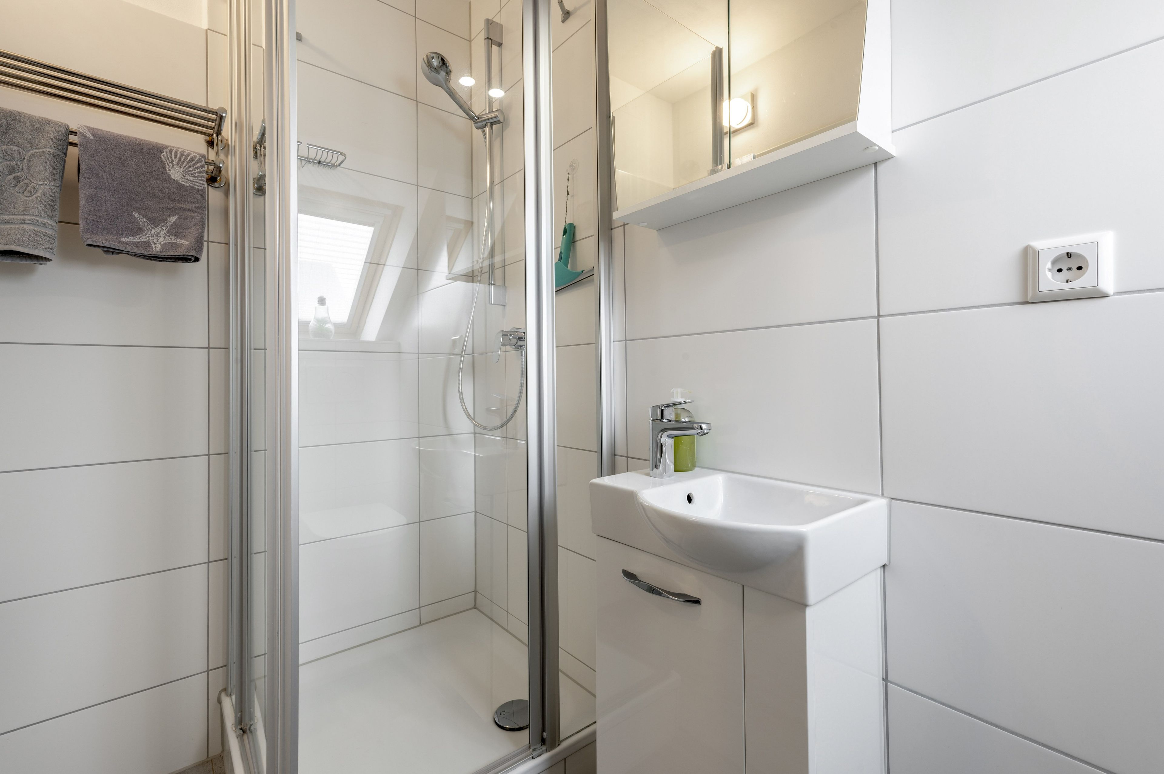 A modern bathroom with a glass shower enclosure, a white sink with a soap dispenser, and a towel rack with towels.