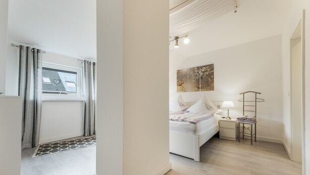 A bedroom with a bed, bedside table, lamp, and a wall-mounted artwork. - Apartment “Seepferdchen” with Wi-Fi (Cuxhaven)