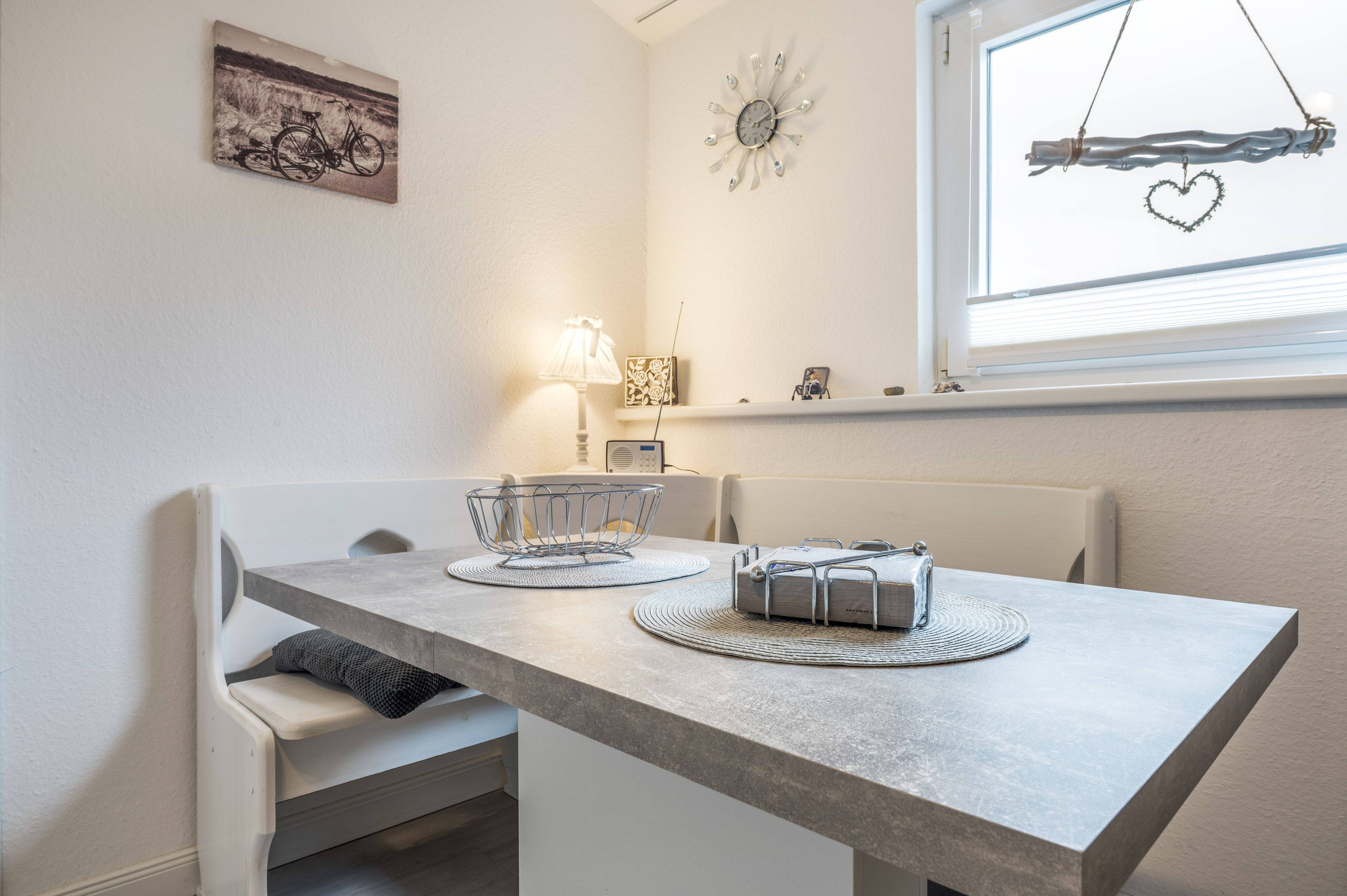 Een eethoek met een tafel, stoelen, een lamp en een wandklok.