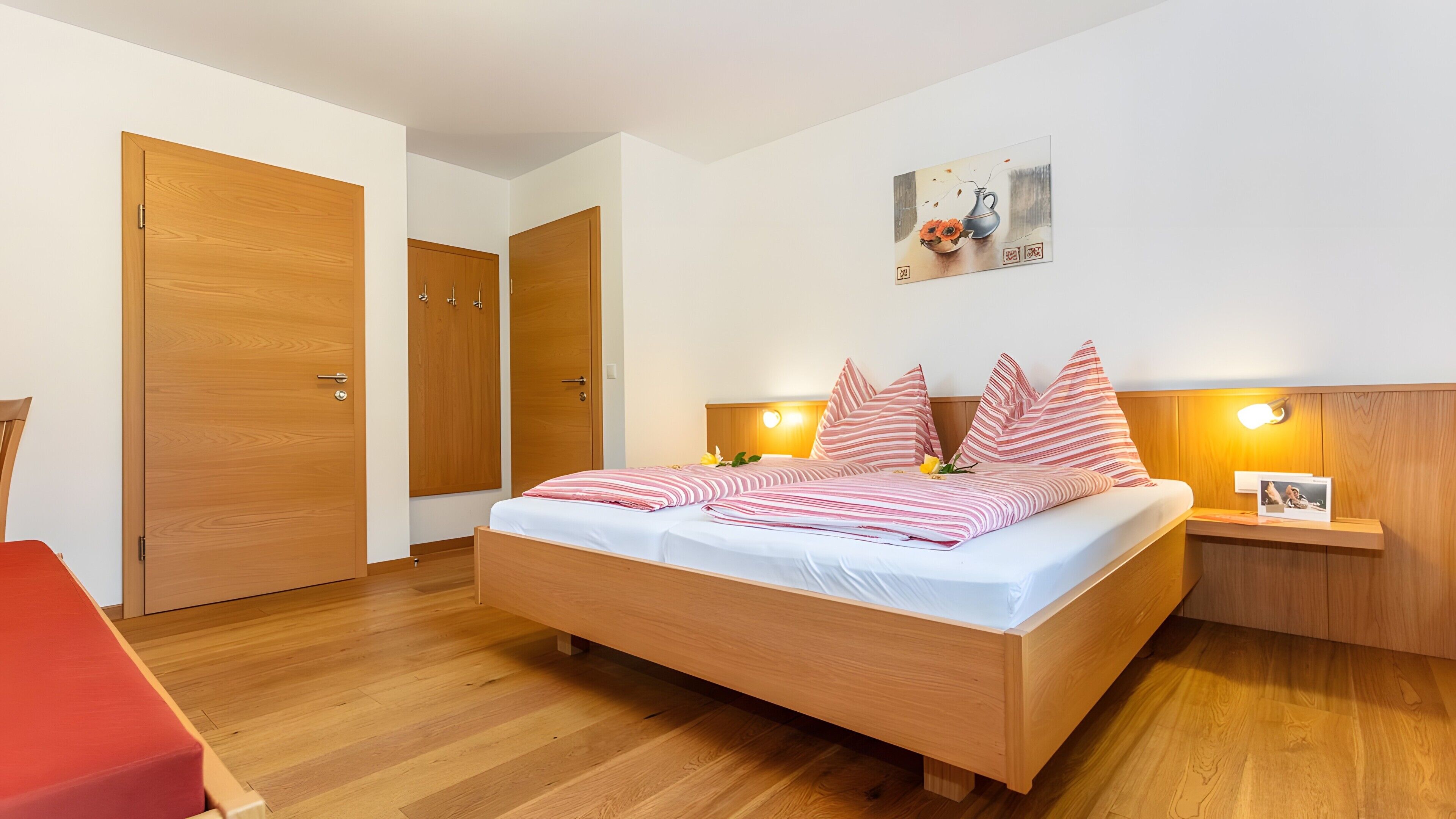 A bedroom with a wooden bed, two bedside tables, a red chair, and a painting on the wall.