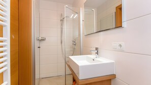 A modern bathroom with a glass shower enclosure, a white sink, and a wooden vanity. - Apartment 'Ferienwohnung Pihapper' with Mountain View, Shared Garden and Wi-Fi (Mittersill)