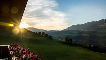 A view of a green landscape with mountains in the distance and a bright sun in the sky.