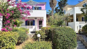 A two-story building with balconies, surrounded by lush greenery and pink bougainvillea flowers.