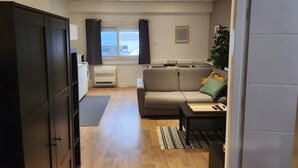 A modern living room with a sofa, a coffee table, a plant, and a kitchen area with a refrigerator and an air conditioner. - Premium Studio – Modern, Functional with Wi-Fi (Saint-Martin-d'Hères)