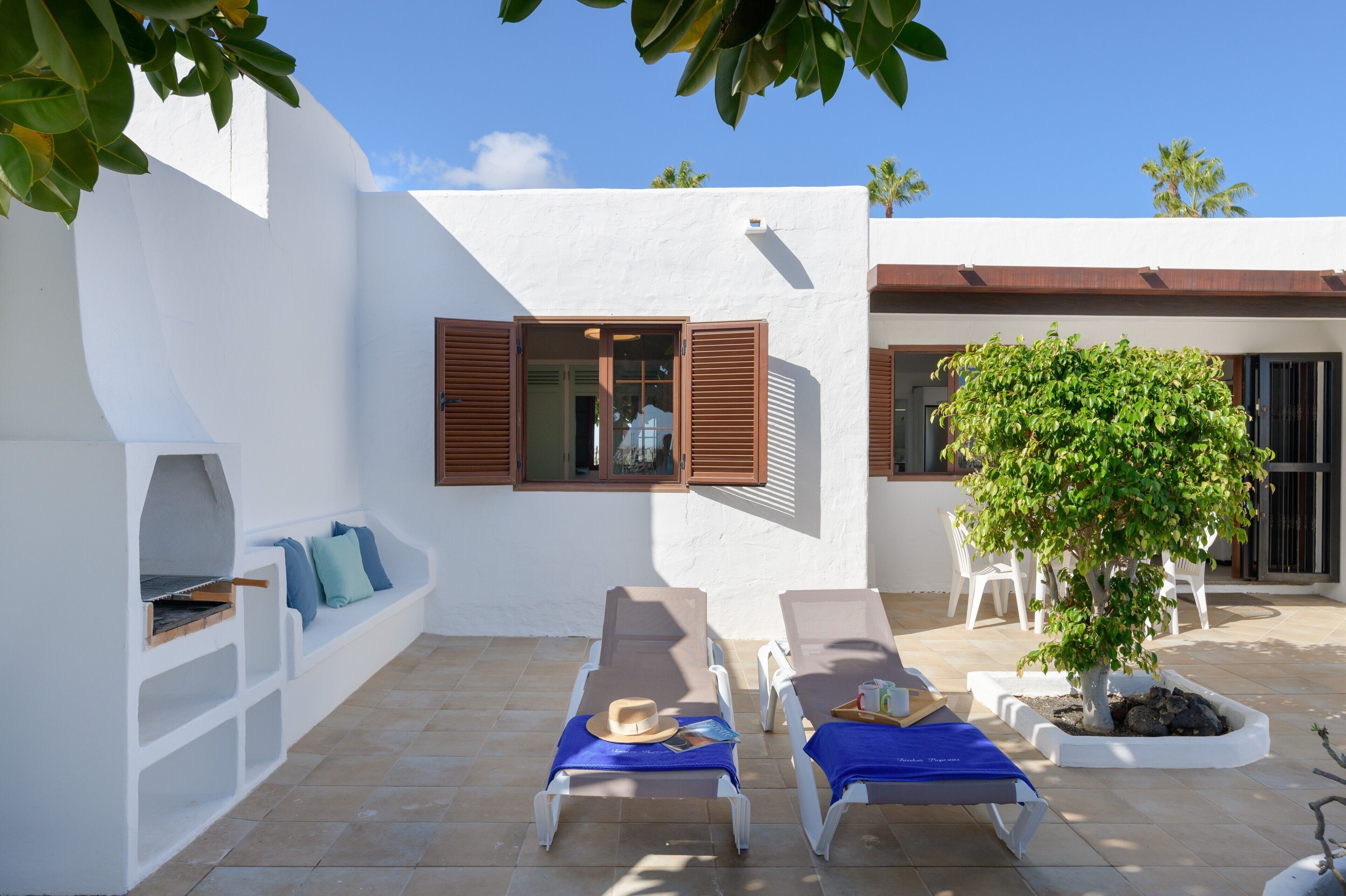 Une terrasse avec deux chaises longues, un barbecue et un arbre en pot.