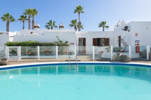 A swimming pool with a clear blue water, surrounded by white buildings with palm trees and a clear sky. - 'Puerto Chico K' with Sea View, Shared Pool and Wi-Fi (Playa Blanca)