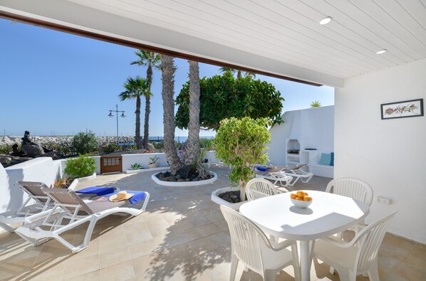A sunlit patio with white furniture, a table with fruit, and a view of the sea. - 'Puerto Chico K' with Sea View, Shared Pool and Wi-Fi (Playa Blanca)