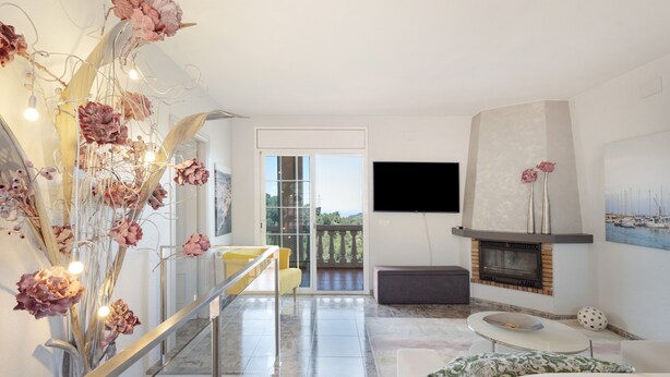 Ein modernes Wohnzimmer mit Kamin, Flachbildfernseher an der Wand und einem Balkon mit Glastür, ergänzt durch ein dekoratives Blumenarrangement.