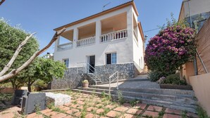 Ein zweigeschossiges Gebäude mit Balkon, Steinstufen und einem Garten mit Kaktee und blühenden Pflanzen.