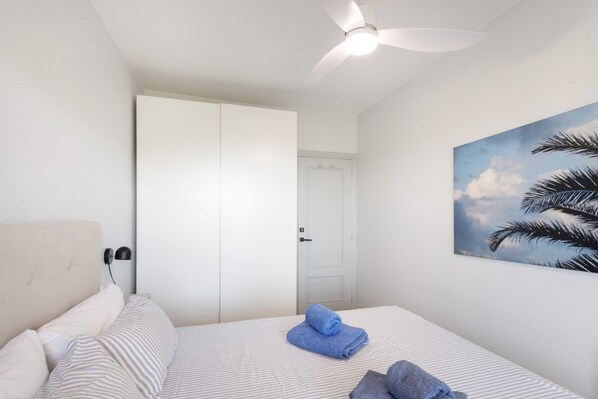 A bedroom with a bed, a ceiling fan, a door, and a wall-mounted painting. - Holiday Home 'Between Forest and Sea' with Sea View, Private Terrace and Wi-Fi (Canyelles)