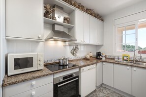 Une cuisine avec des meubles blancs, un four à micro-ondes, un four traditionnel, un lave-vaisselle et une fenêtre donnant sur un beau paysage.