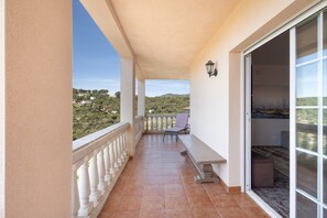 A balcony with a view of a hilly landscape, a bench, a table, and a sliding glass door. - Holiday Home 'Between Forest and Sea' with Sea View, Private Terrace and Wi-Fi (Canyelles)