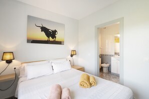 Et hotelværelse med en seng, to sengeborde, en billed af en tyr og et badeværelse, der kan ses gennem en åben dør.