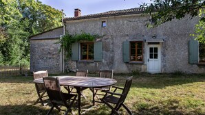 A rustic stone building with a round wooden table and chairs, a white door, and green shutters. - Holiday Home "Gîte De Chez Chenon" with Private Garden (Saint-Sulpice-de-Ruffec)