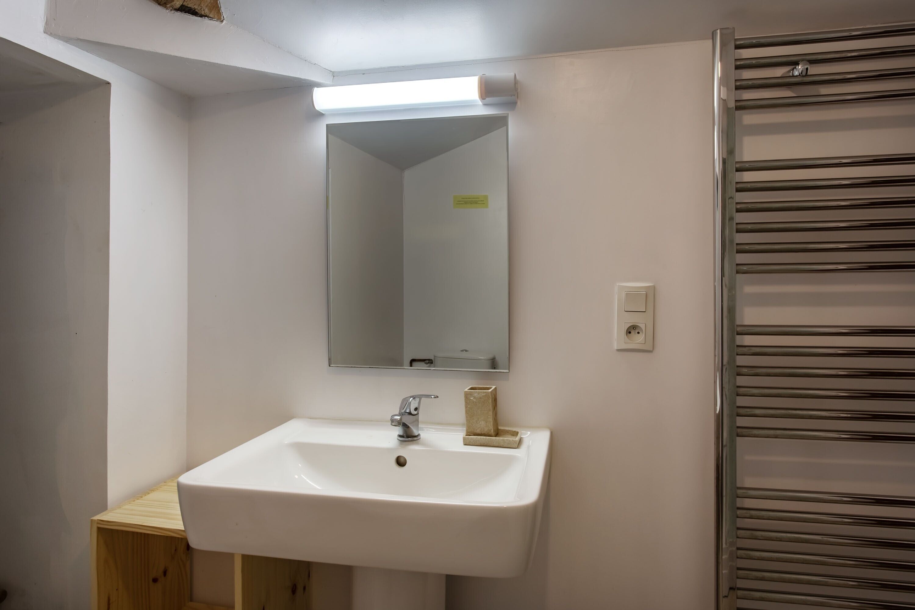 A bathroom with a white sink, a mirror, a towel dispenser, and a towel rack.