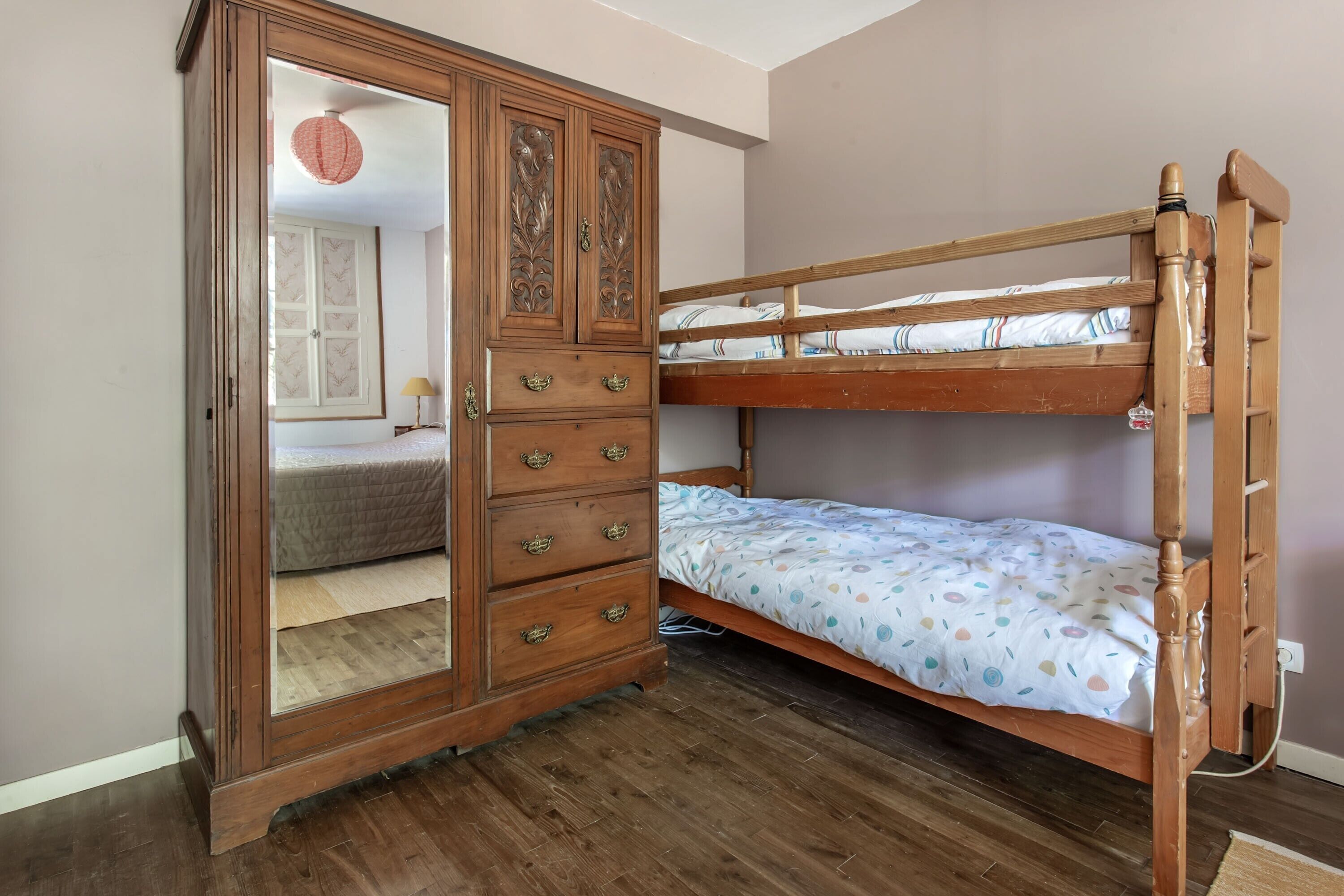 A bunk bed with a wooden frame and a wardrobe with multiple drawers and a mirror.