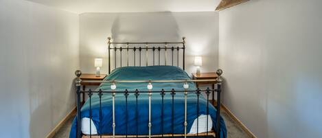 A single bed with a metal frame, two bedside tables, and a green bedspread.