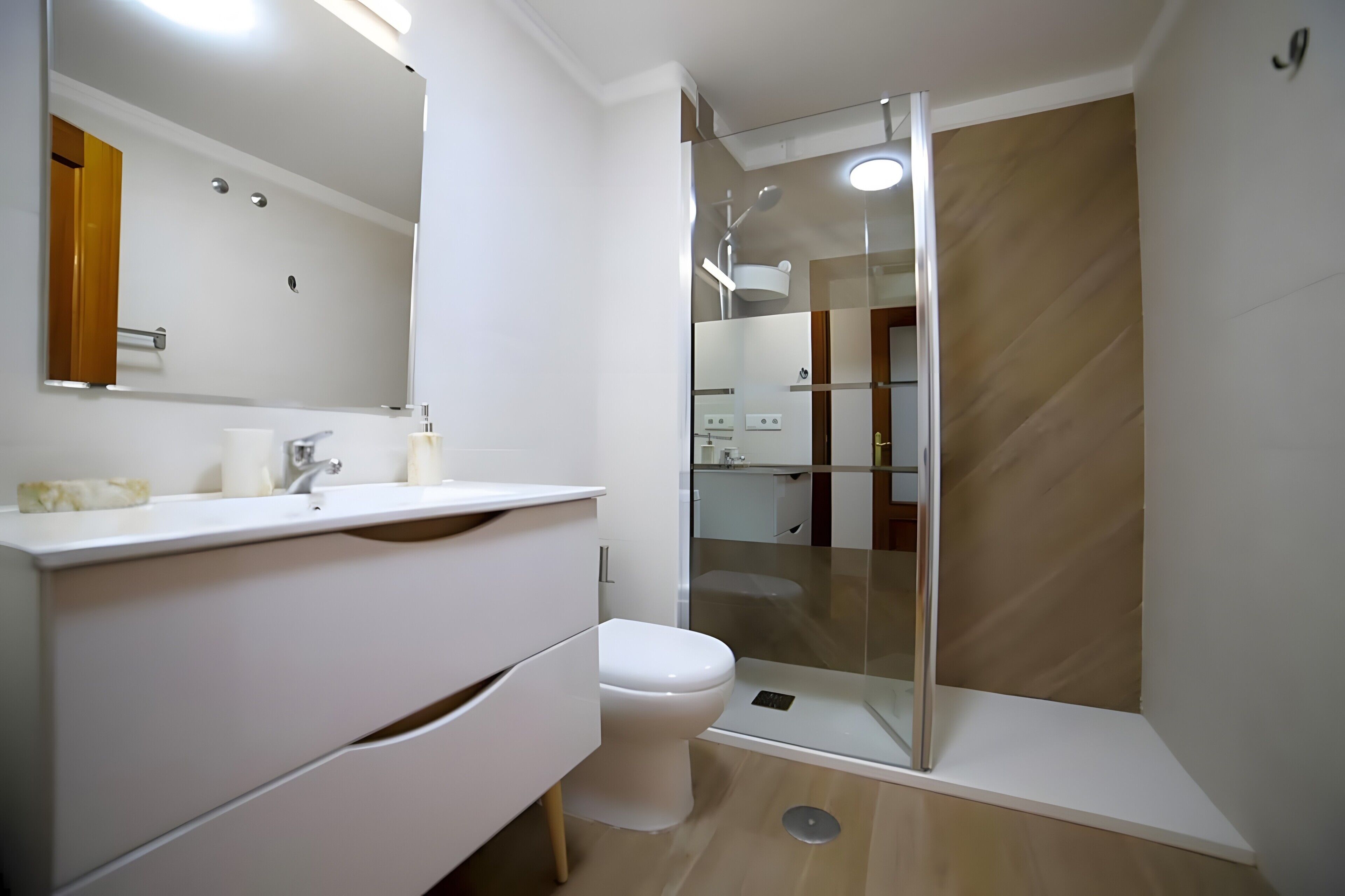 Ein modernes Badezimmer mit einer Glaskabine zur Dusche, einem weißen Waschbecken mit Marmorplatte und einem großen Spiegel.