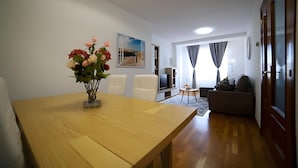 A living room with a wooden table, a sofa, a TV, and a painting on the wall. - Apartment 'Playa Arbeyal Garaje' with Wi-Fi (Gijón)