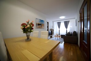 Een woonkamer met een houten tafel, een bank, een televisie en een schilderij aan de muur.