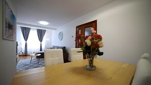 A living room with a wooden dining table, a vase with flowers, a sofa, and a dining table set with a glass and a plate. - Apartment 'Playa Arbeyal Garaje' with Wi-Fi (Gijón)