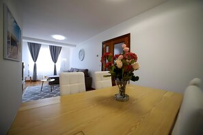Een woonkamer met een houten eettafel, een vaas met bloemen, een bank en een eettafel gedekt met een glas en een bord.