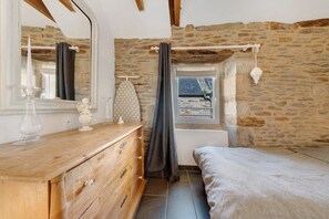 A bedroom with a stone wall, wooden dresser, and a bed. - Rental in Le Conquet Near Beaches and Shops (Le Conquet)