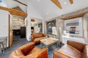 Amplia sala de estar con sofás de cuero, una mesa de centro de madera, paredes de piedra y una chimenea.