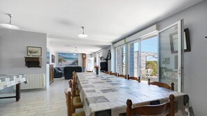 A dining area with a long table, chairs, and a view through glass doors.