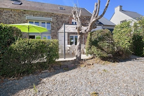 A stone building with a patio area, outdoor seating, and a tree in the foreground.