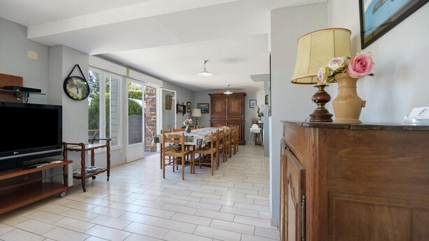 A spacious living area with a television, dining table, chairs, and a wooden cabinet.