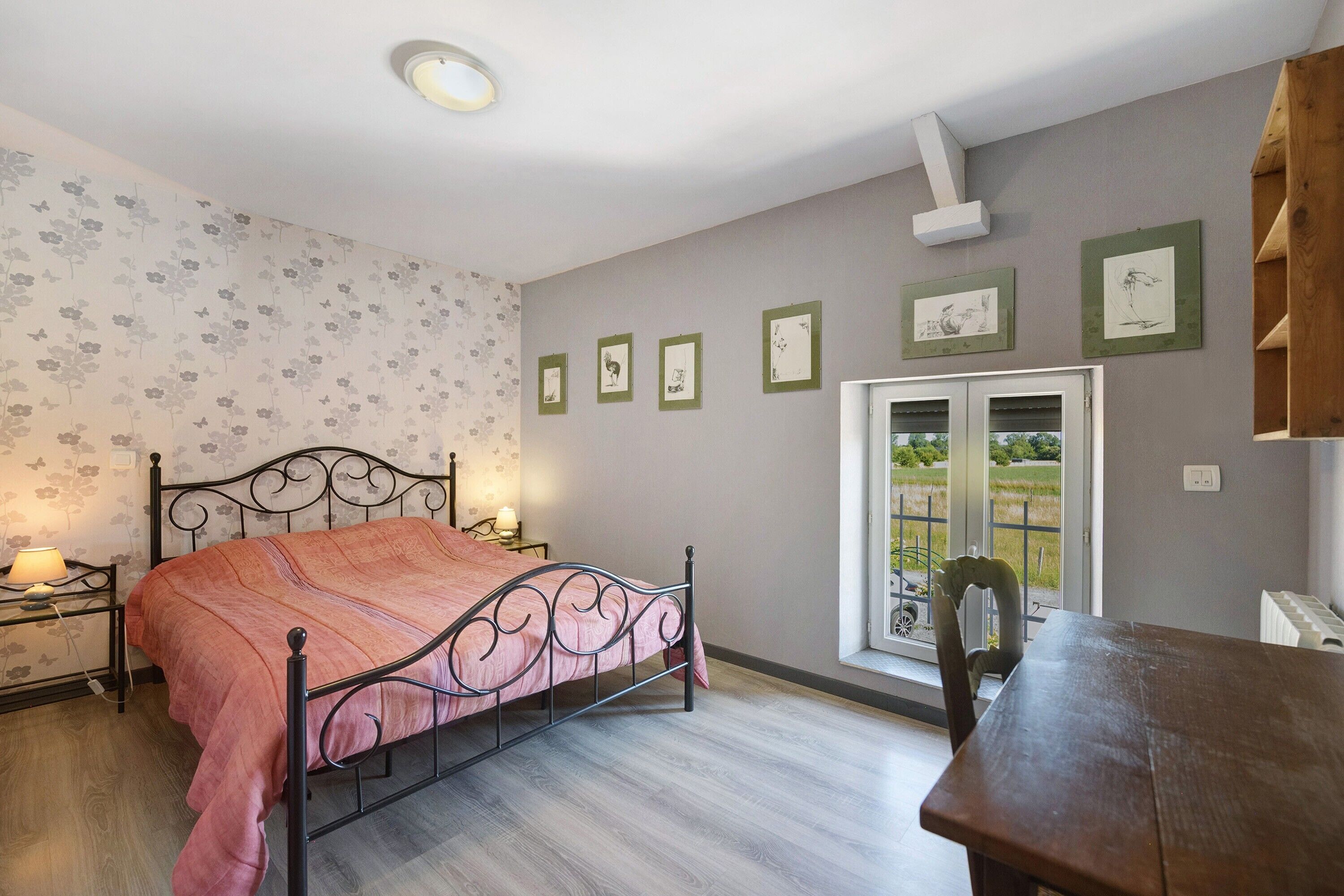 A bedroom with a bed, bedside tables, a window with a view, and framed pictures on the wall.