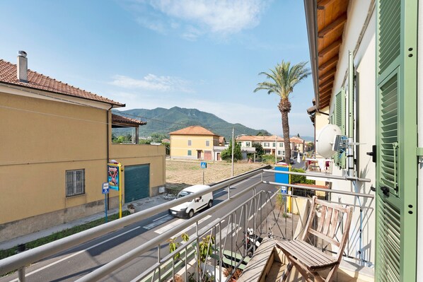 A balcony with a view of a street, a palm tree, and a mountain in the background. - Room 'Leone' with Mountain View, Wi-Fi and Air Conditioning (Bastia)