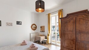 A bedroom with a bed, a wooden wardrobe, a table with a chair, a radiator, and a window with curtains. - Room 'Leone' with Mountain View, Wi-Fi and Air Conditioning (Bastia)
