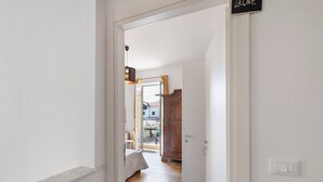 A hallway leading to a bedroom with a bed, a wooden wardrobe, and a lit switch on the wall. - Room 'Leone' with Mountain View, Wi-Fi and Air Conditioning (Bastia)
