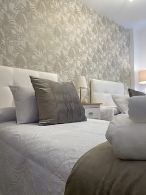 Ein Hotelzimmer mit gestreiftem Wandpapier, einem Bett mit vielen Kissen, einem Nachttisch mit Lampe und einem zusätzlichen Beistelltisch.