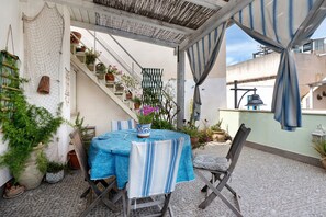 Eine Terrasse im Freien mit Tisch und Stühlen, Blumentöpfen, einer Treppe und einer Pergola.