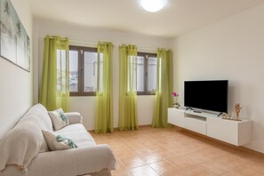 Ein Wohnzimmer mit einer Couch, einem Fernseher auf einem weißen Schrank und grünen Vorhängen.