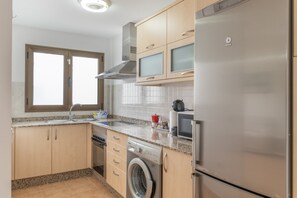Eine Küche mit Holzschränken, einem Edelstahlkühlschrank, einer Waschmaschine und einer Mikrowelle.